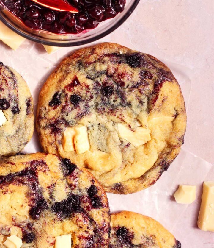 white chocolate chunk lemon blueberry cookies on parchment with bowl of blueberry sauce
