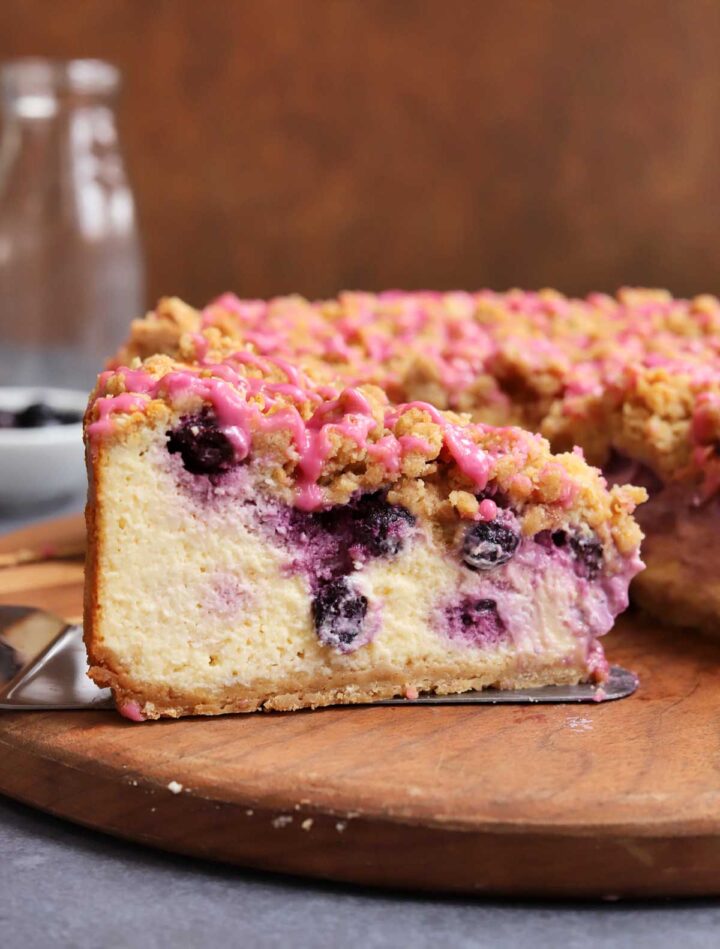 slice of blueberry crumble cheesecake on cutting board showing creamy inside