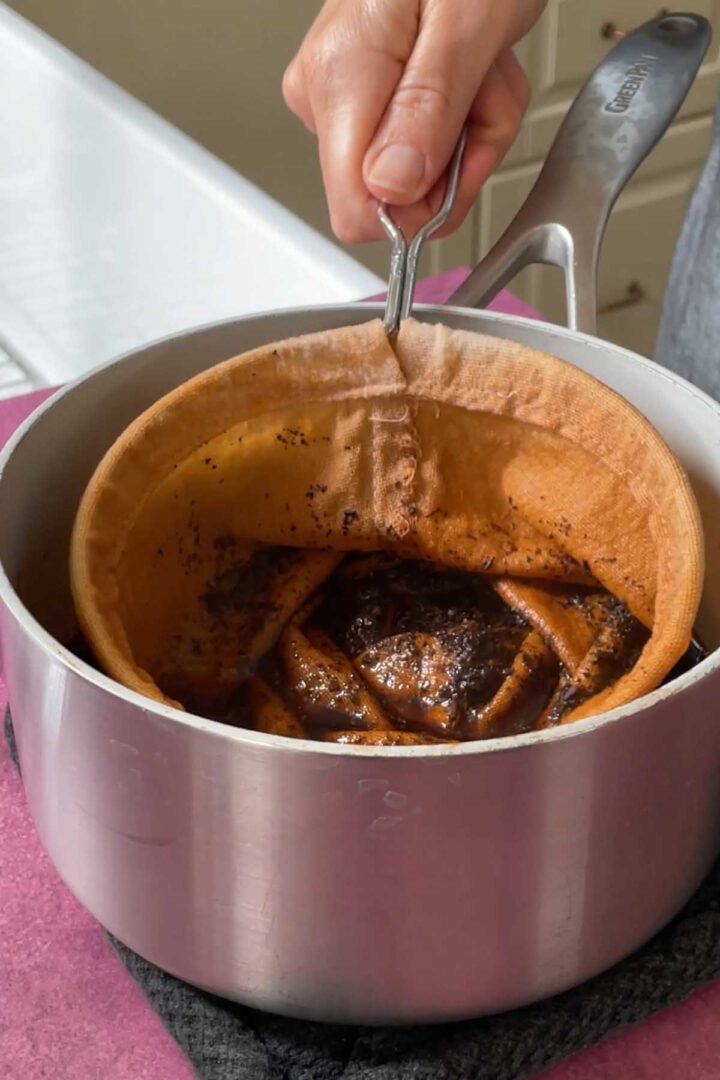 straining Thai tea leaves through tea sock into saucepan