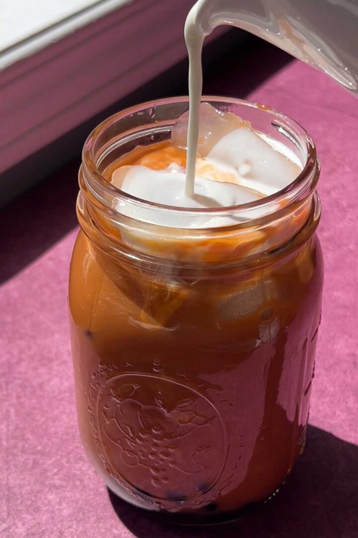 pouring milk over iced Thai tea in glass