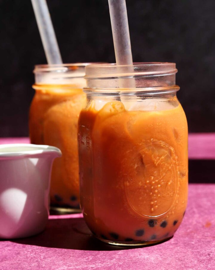 two glasses of Thai tea bubble tea with boba straw and jug of milk