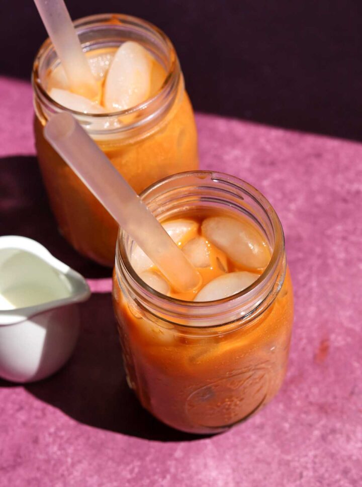 top angle view of two glasses of Thai tea bubble tea with boba straw and jug of milk
