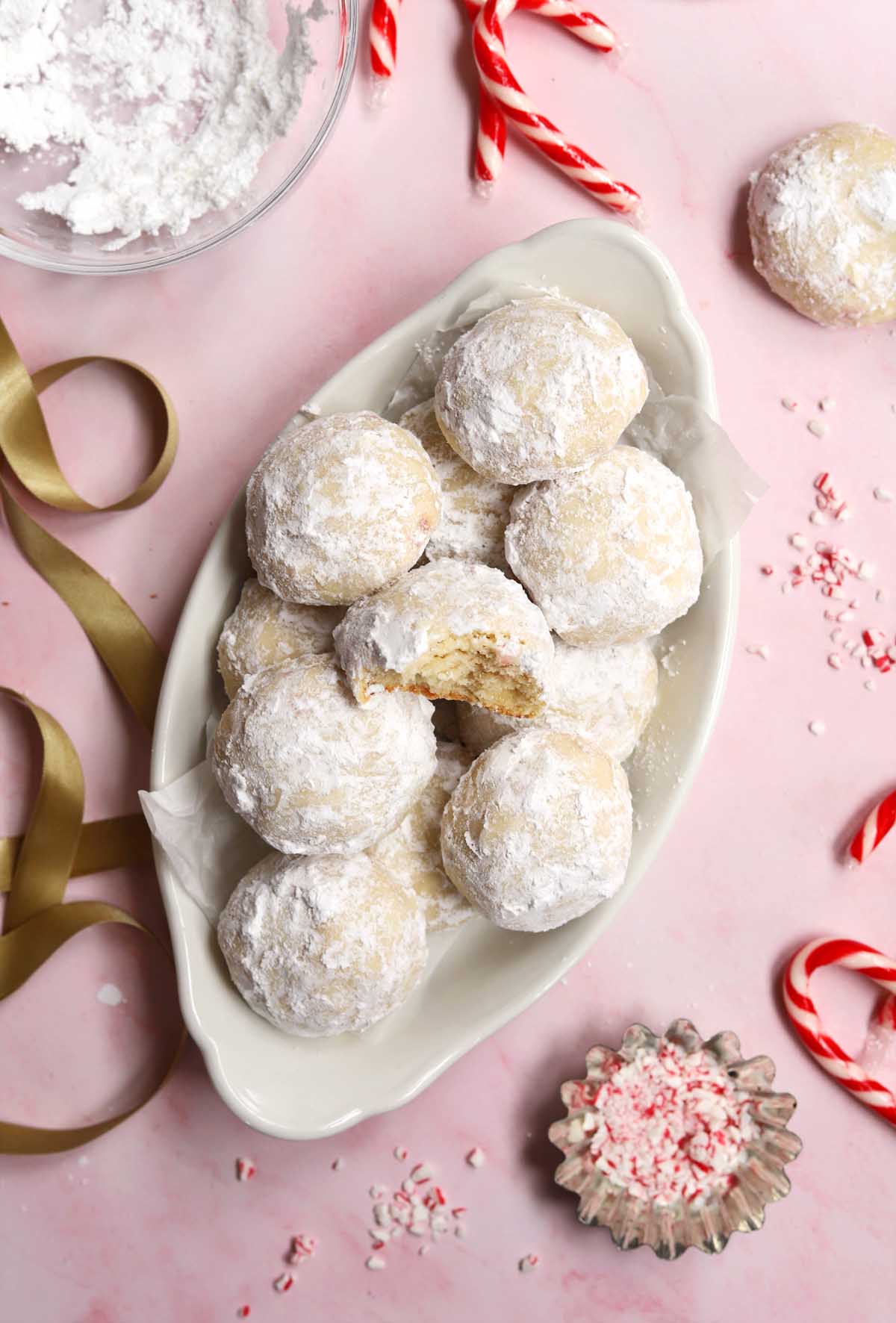 top view of peppermint snowball cookies in a serving dish with bite showing tender insides