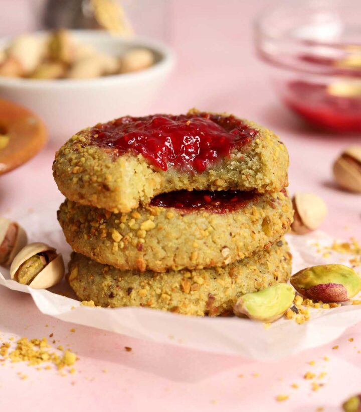 stack of raspberry pistachio thumbprint cookies with bite