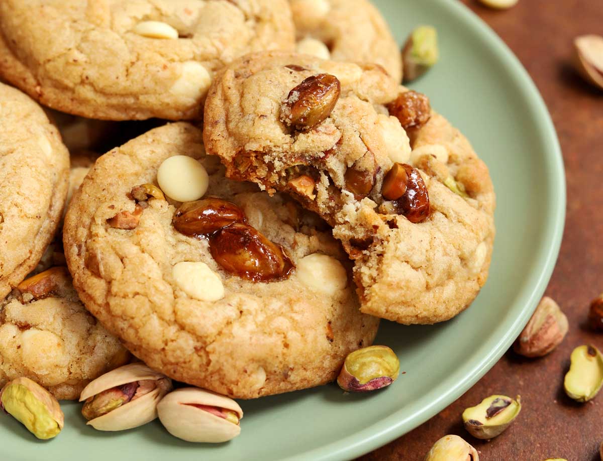 side view of caramelized pistachio brown butter white chocolate cookies on a plate with bite