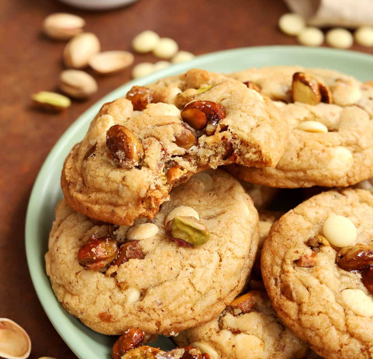 side view of caramelized pistachio brown butter white chocolate cookies on a plate with bite