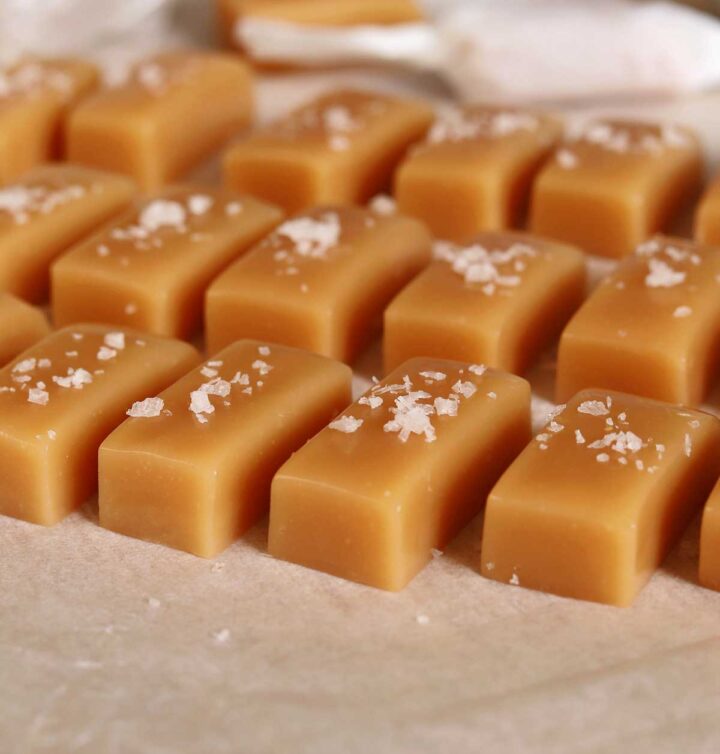 homemade buttery soft caramels lined up on cutting board with flaky sea salt