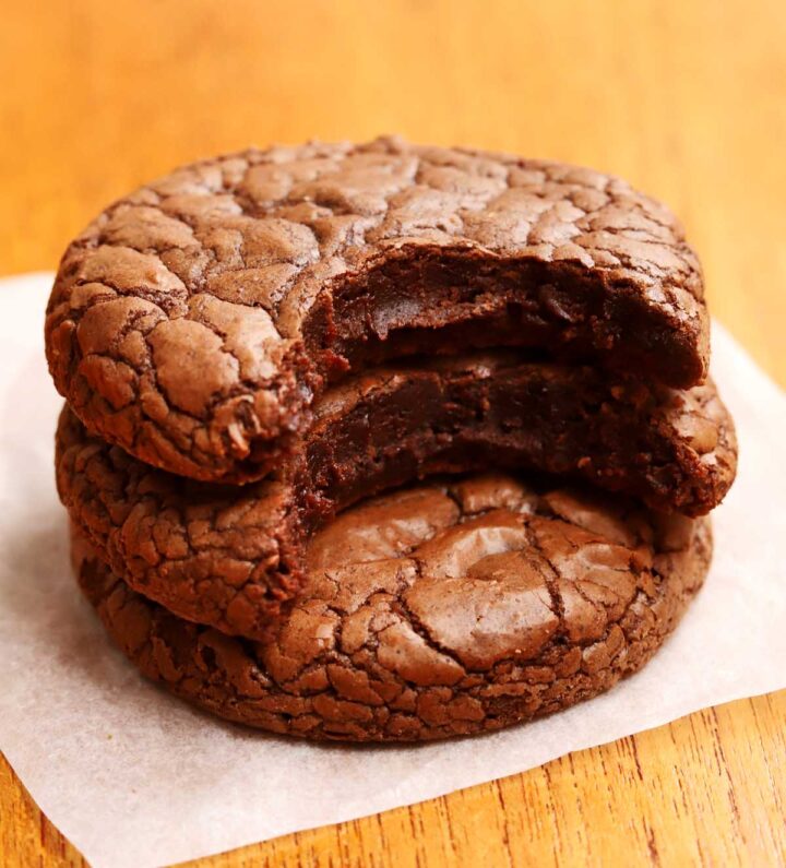 fudgy brownie cookies stacked on parchment with bite showing fudgy texture