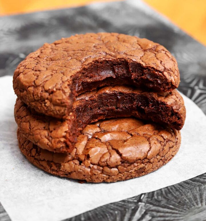 fudgy brownie cookies stacked on parchment with bite showing fudgy texture