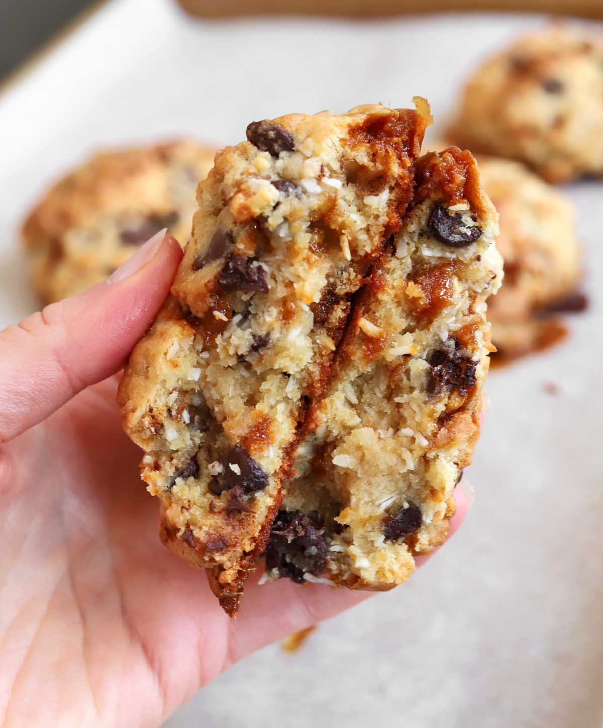 hand holding levain bakery caramel coconut cookie broken in half showing chewy center