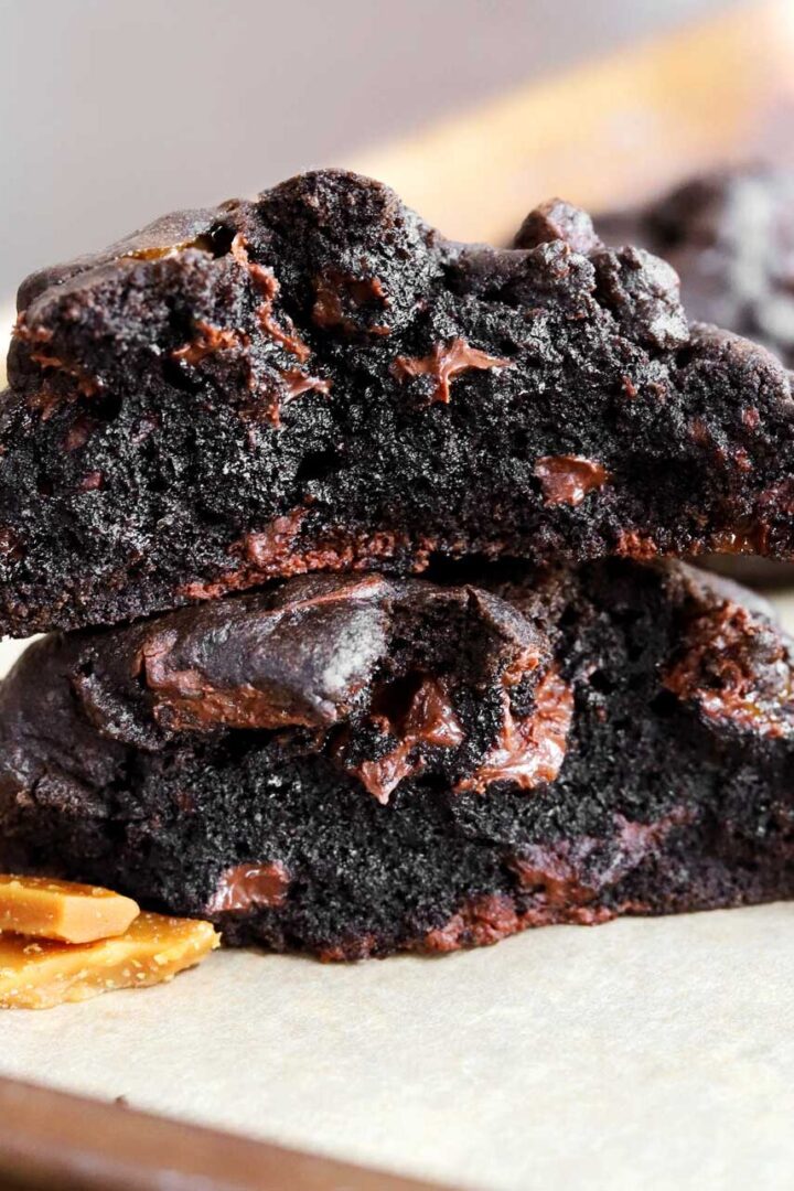 levain bakery coffee toffee cookies broken in half and stacked on a baking sheet showing fudgy interior