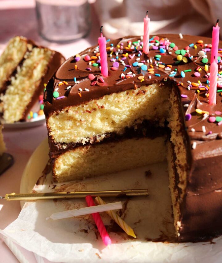 classic vanilla birthday cake on serving plate, sliced with birthday candles