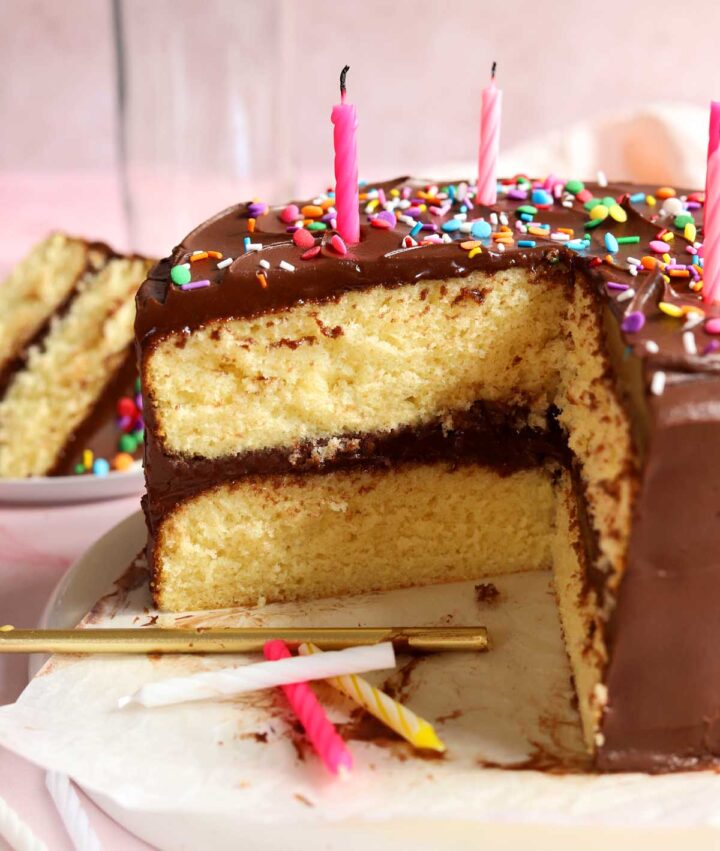 classic vanilla birthday cake on serving plate, sliced with birthday candles