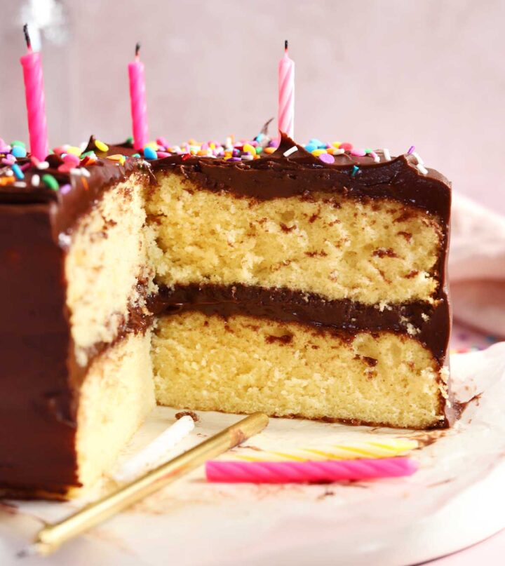 classic vanilla birthday cake on serving plate, sliced with birthday candles