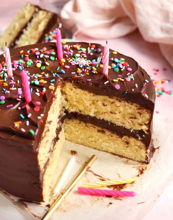 classic vanilla birthday cake on serving plate, sliced with birthday candles