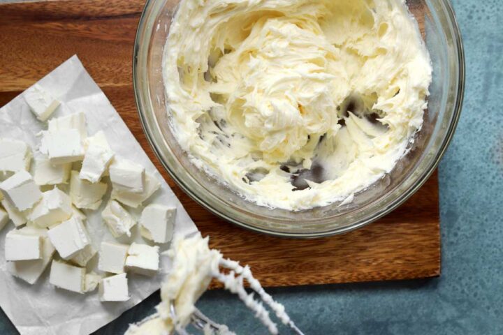 making cream cheese frosting by adding cubes of cream cheese slowly to whipped butter and sugar