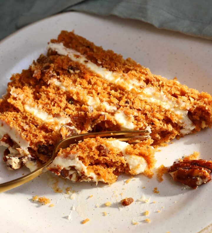 slice of praline crunch carrot cake layer cake on a plate with fork and bite