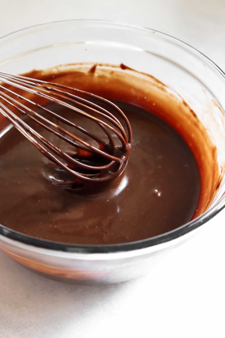 glossy milk chocolate frosting base in a bowl with whisk