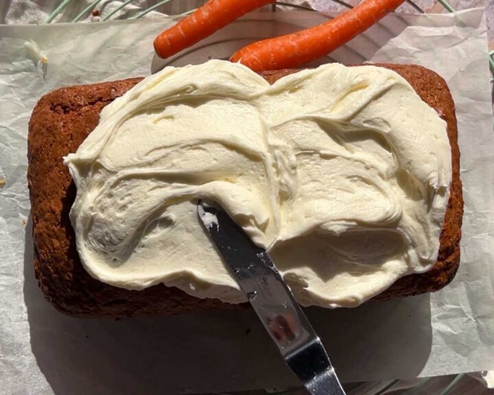spreading cream cheese frosting over cooled carrot cake loaf cake