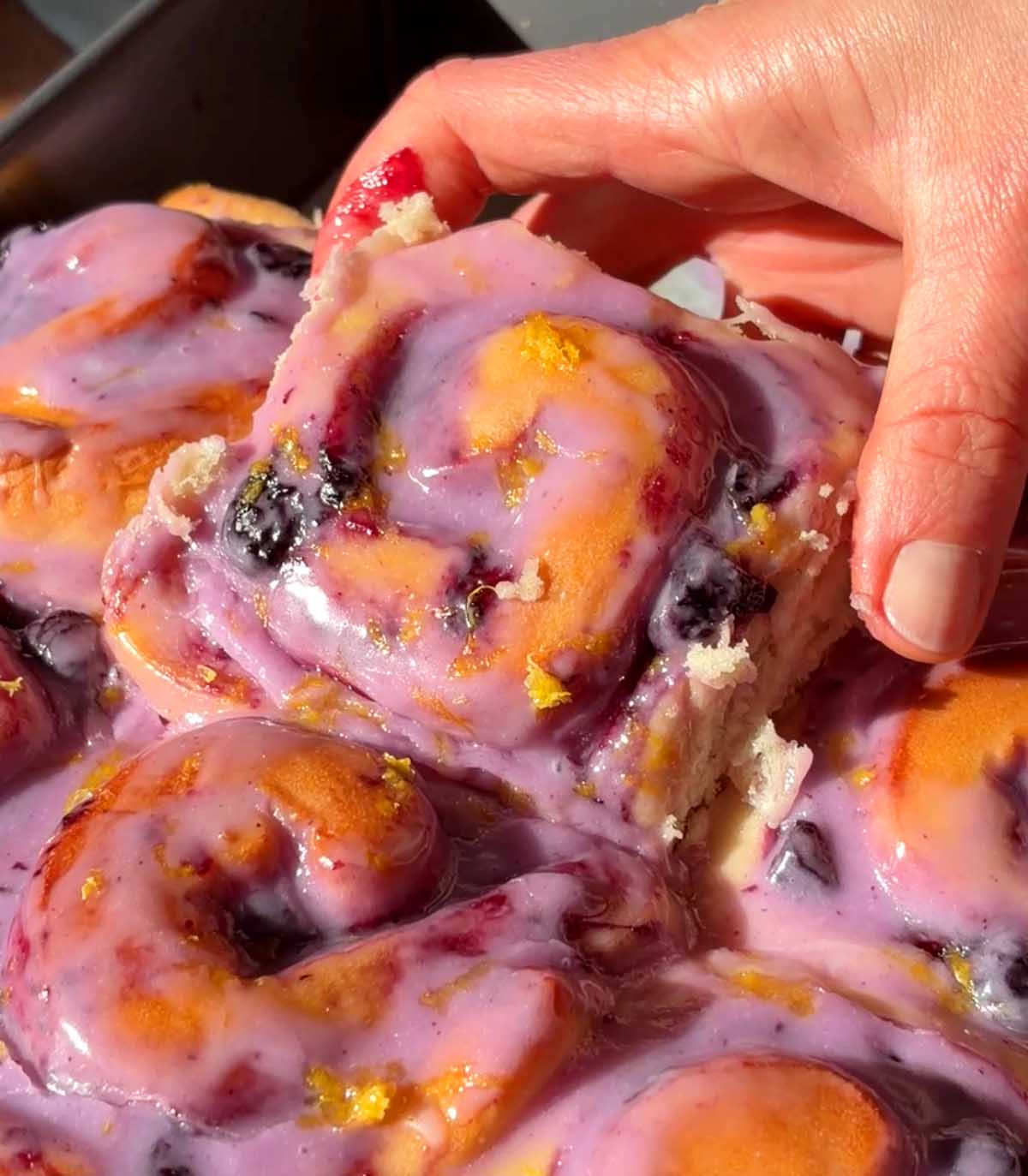 pulling up a roll of lemon blueberry sweet rolls in baking pan
