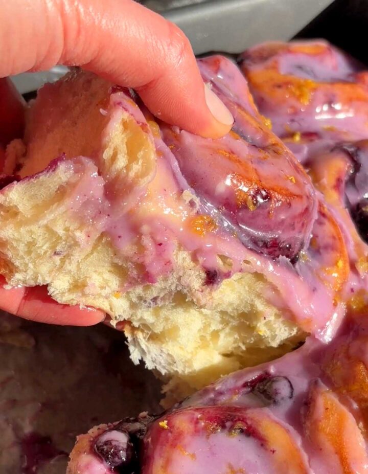 pulling up a roll of lemon blueberry sweet rolls in baking pan