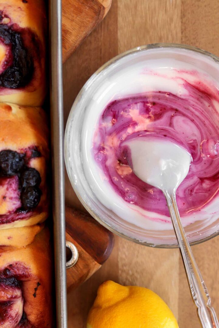 lemon blueberry sweet rolls in baking pan with bowl of blueberry icing