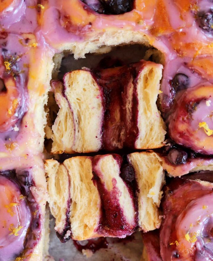 close up of lemon blueberry sweet rolls in baking pan with one roll split open showing fluffy texture