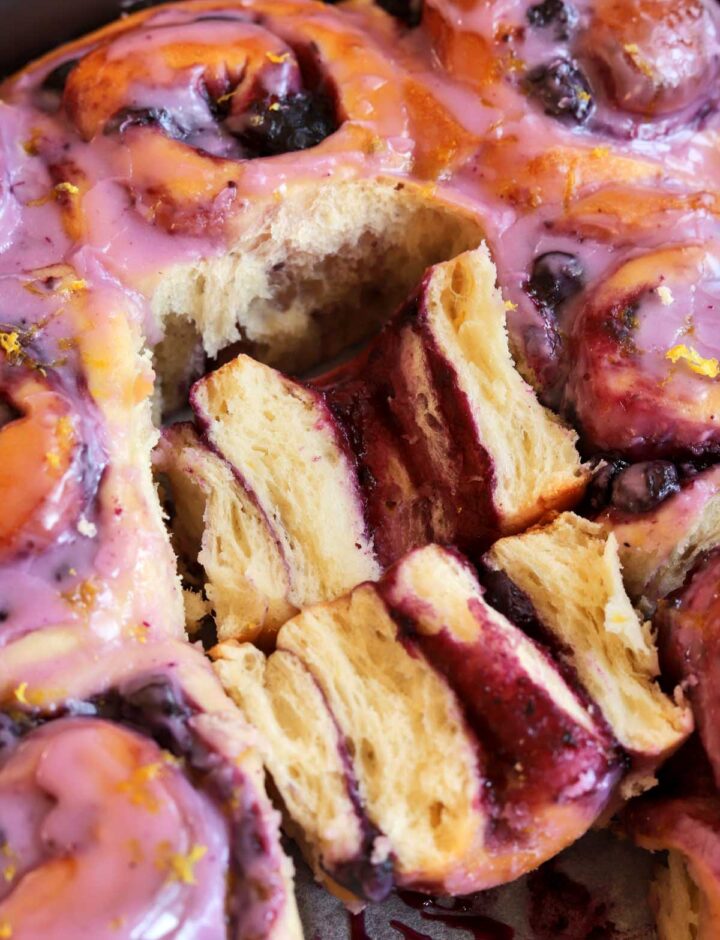 close up of lemon blueberry sweet rolls in baking pan with one roll split open showing fluffy texture