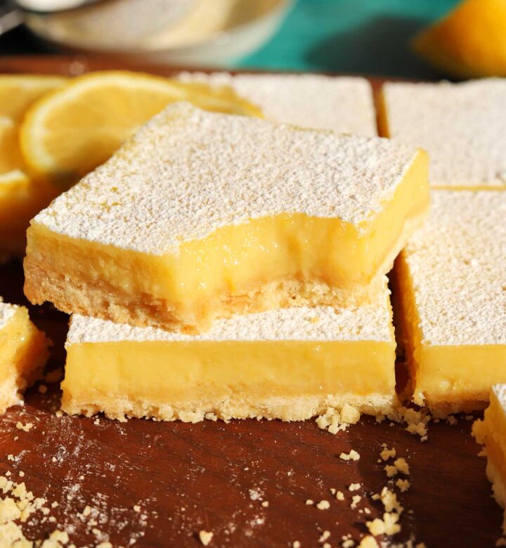 creamy lemon bars stacked on cutting board with bite