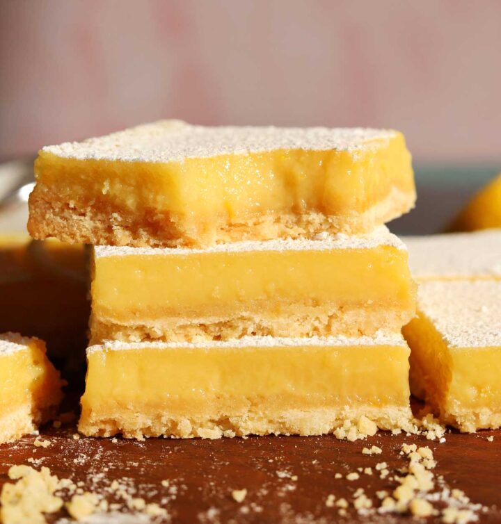 creamy lemon bars stacked on cutting board with bite