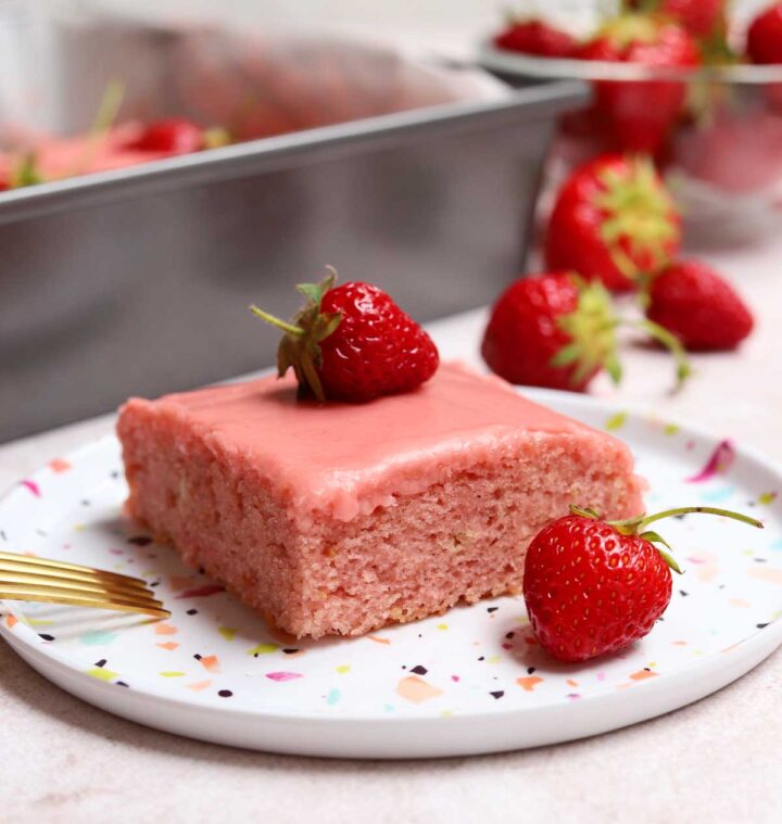 slice of strawberry sheet cake on a plate with fresh strawberries