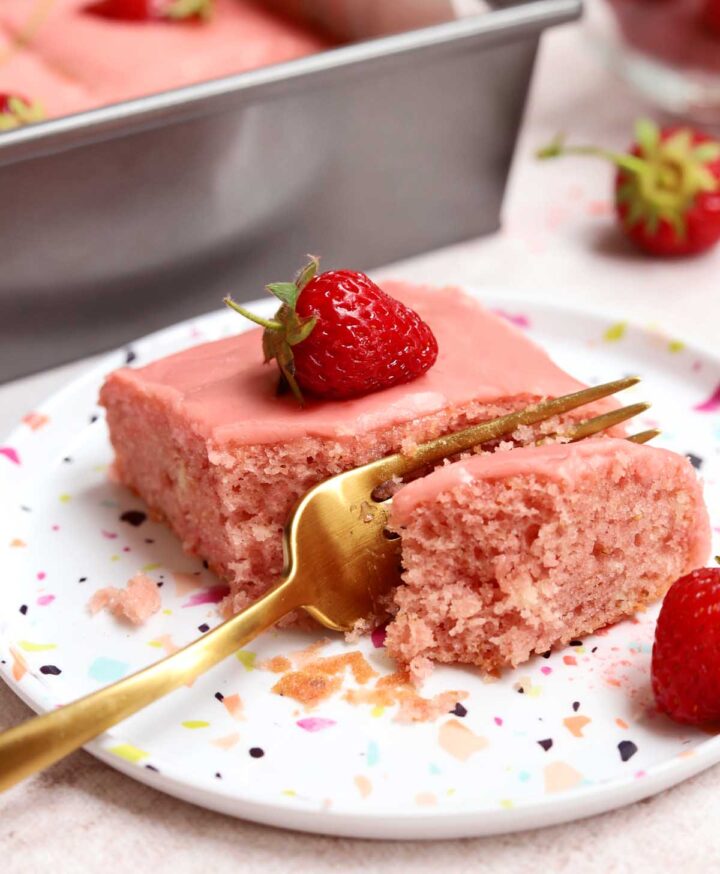 slice of strawberry sheet cake on a plate with bite and fork