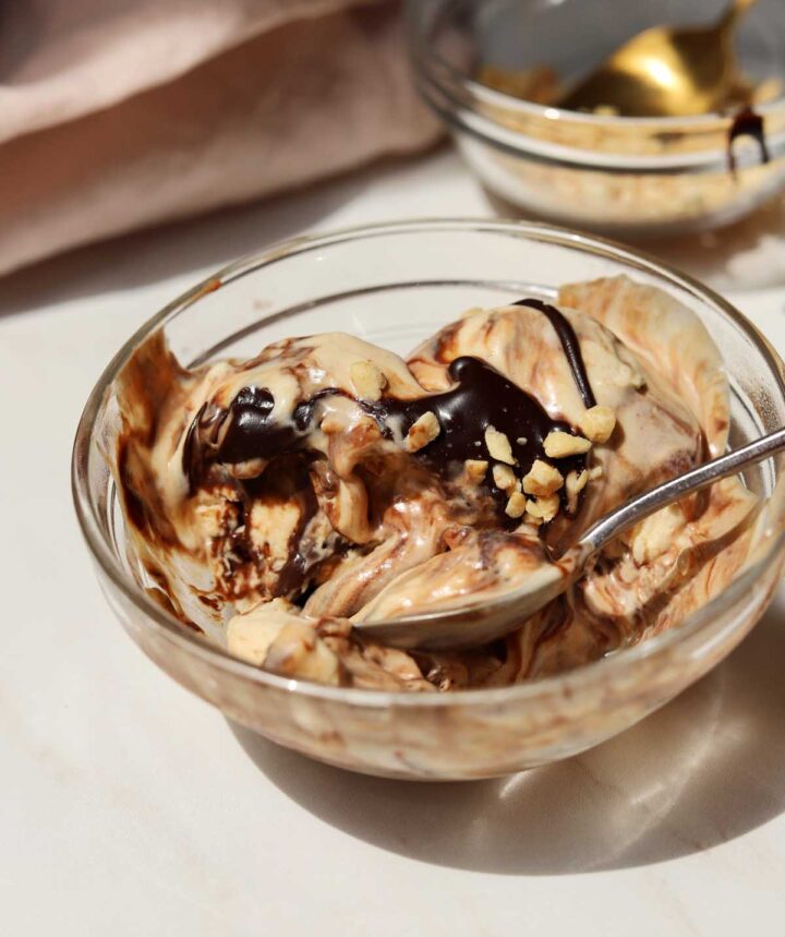 scoops of no churn peanut butter espresso fudge ice cream in a bowl with hot fudge sauce and peanuts