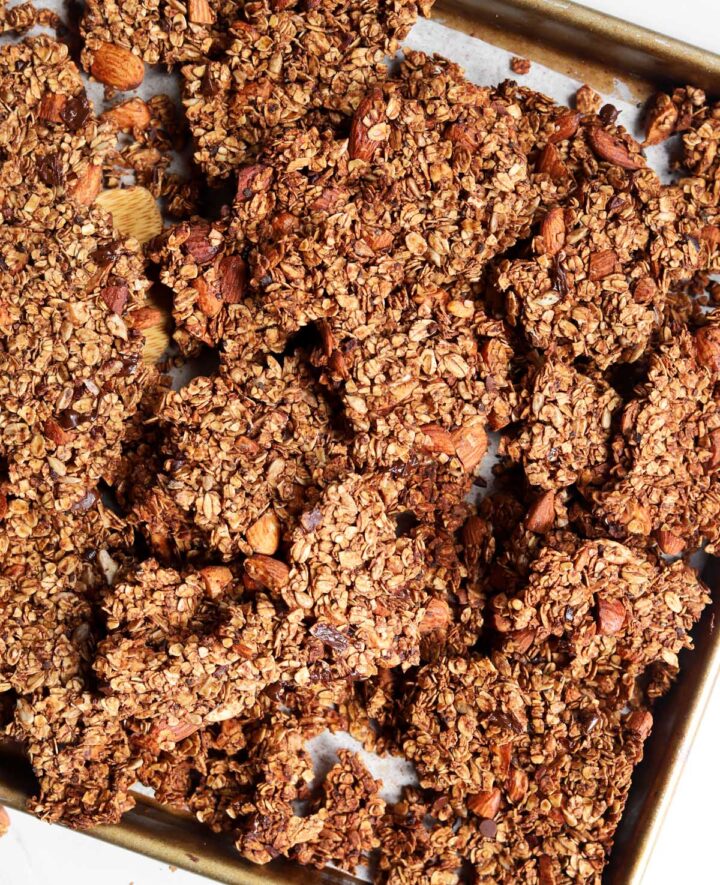 chocolate olive oil granola on a baking sheet with wooden spatula