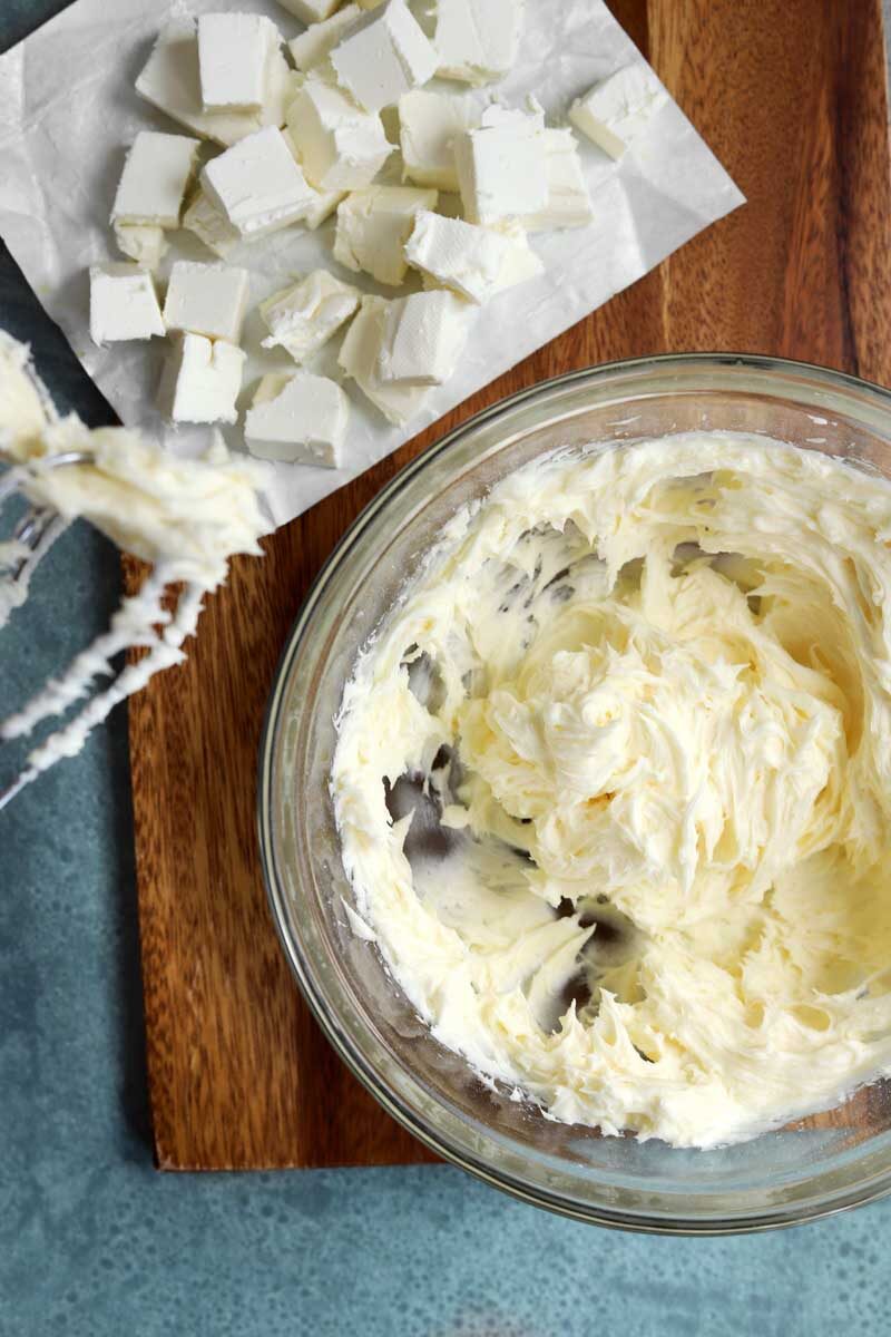 making cream cheese frosting by adding cubes of cream cheese slowly to whipped butter and sugar