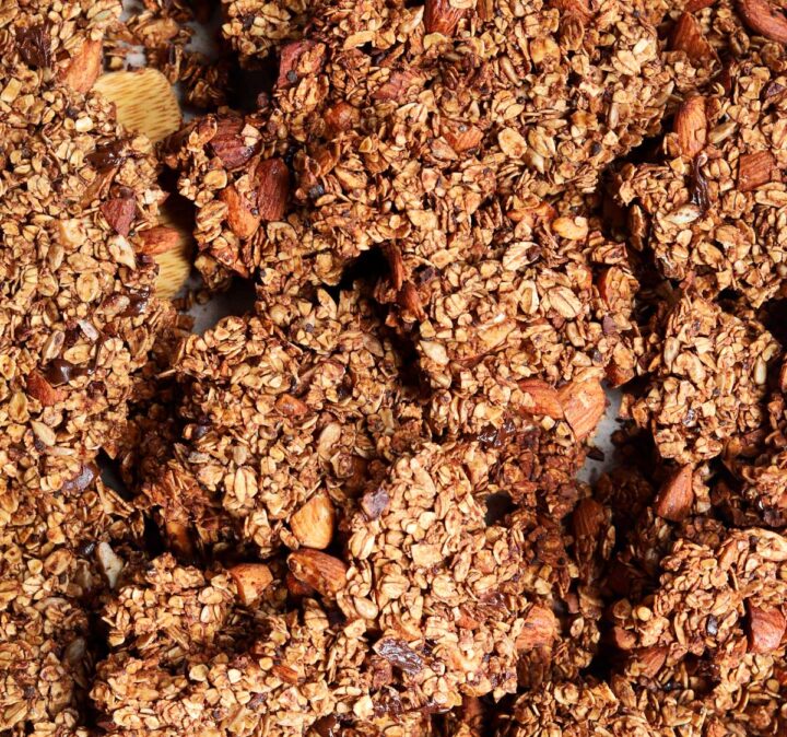 chocolate olive oil granola on a baking sheet with wooden spatula