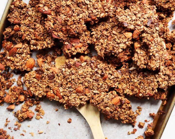 chocolate olive oil granola on a baking sheet with wooden spatula