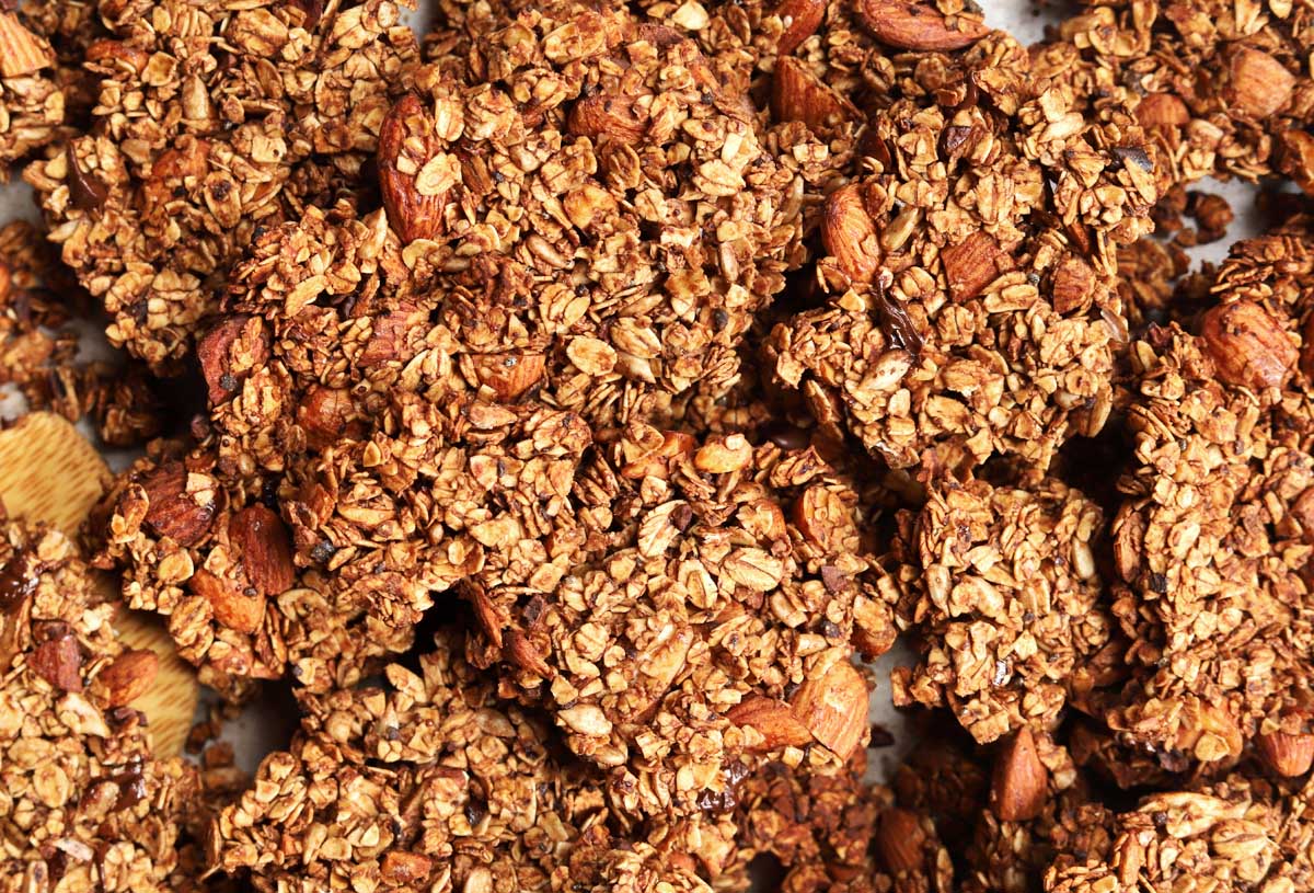 chocolate olive oil granola on a baking sheet with wooden spatula