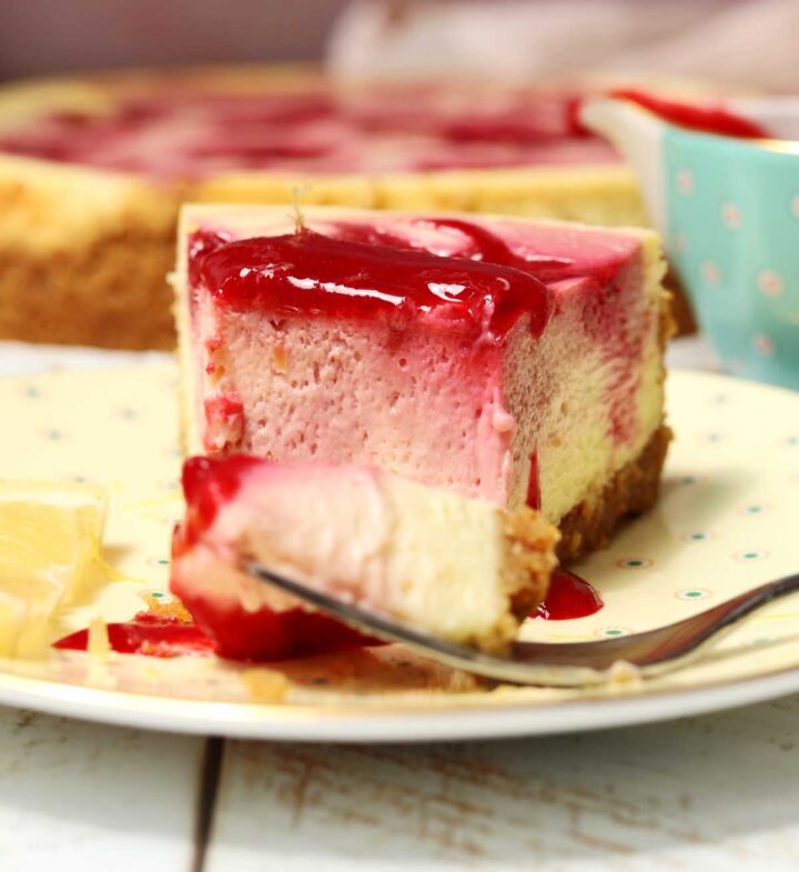 raspberry lemonade cheesecake slice on a plate with raspberry sauce and bite on a fork
