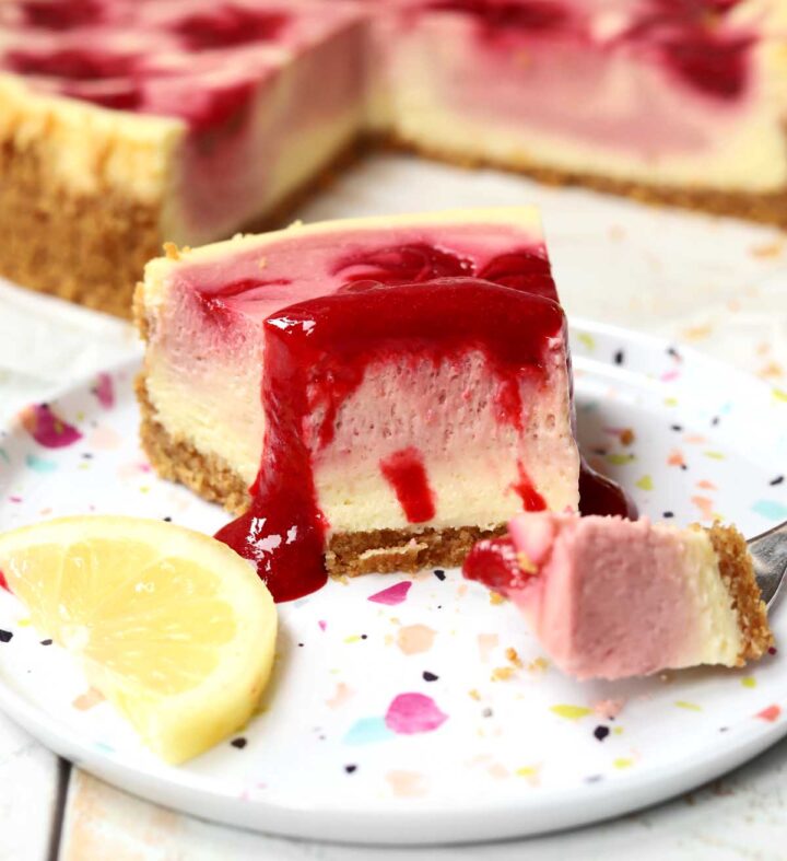 lemon raspberry cheesecake slice on a plate with raspberry sauce and bite on a fork