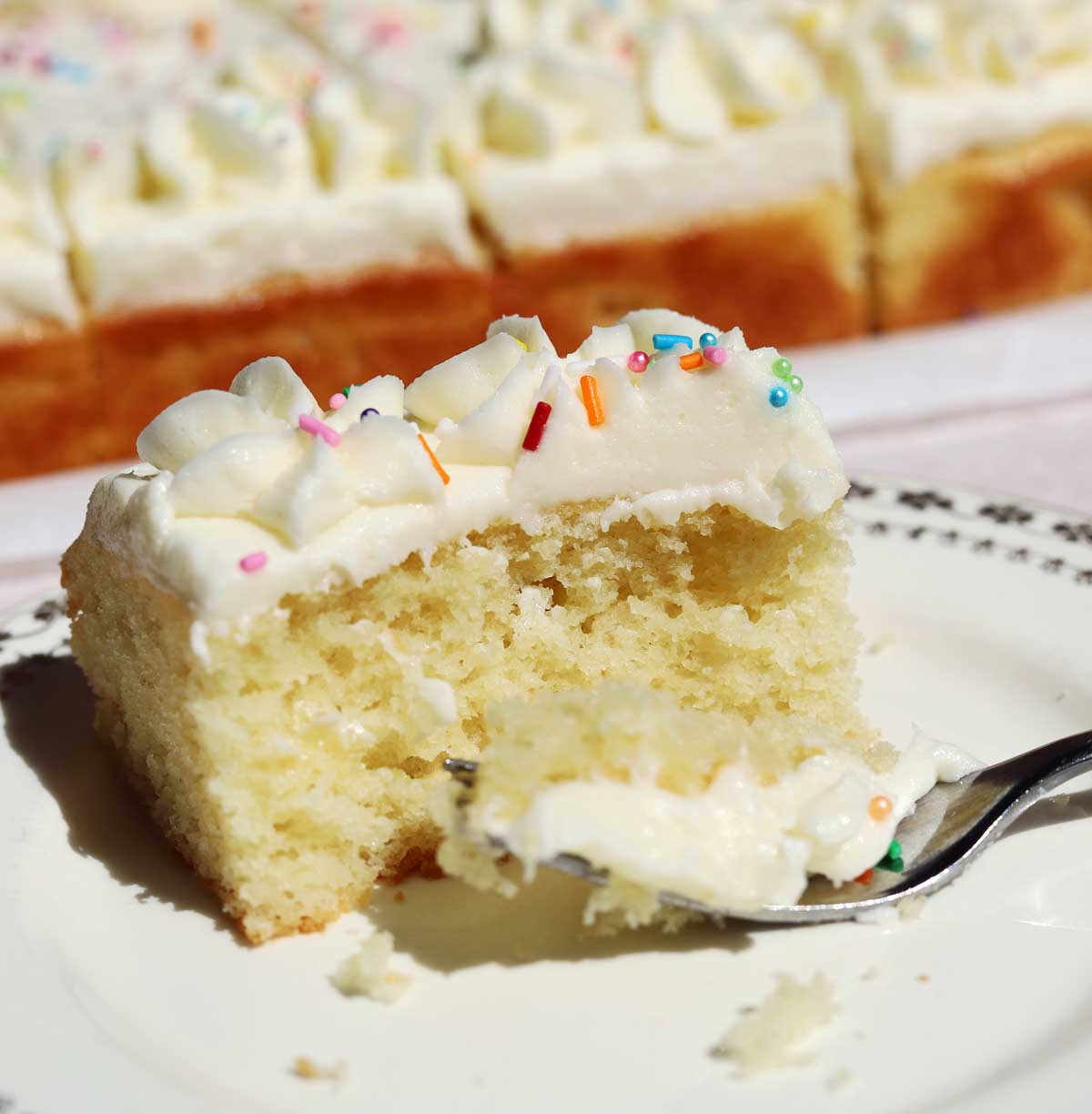 slice of moist vanilla sheet cake on a plate with bite and fork