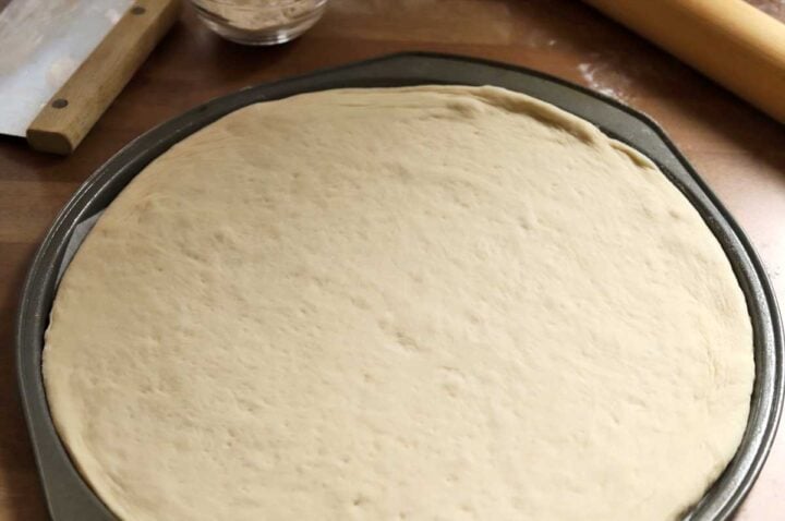 homemade pizza dough rolled out in pan for second proof to make pizza