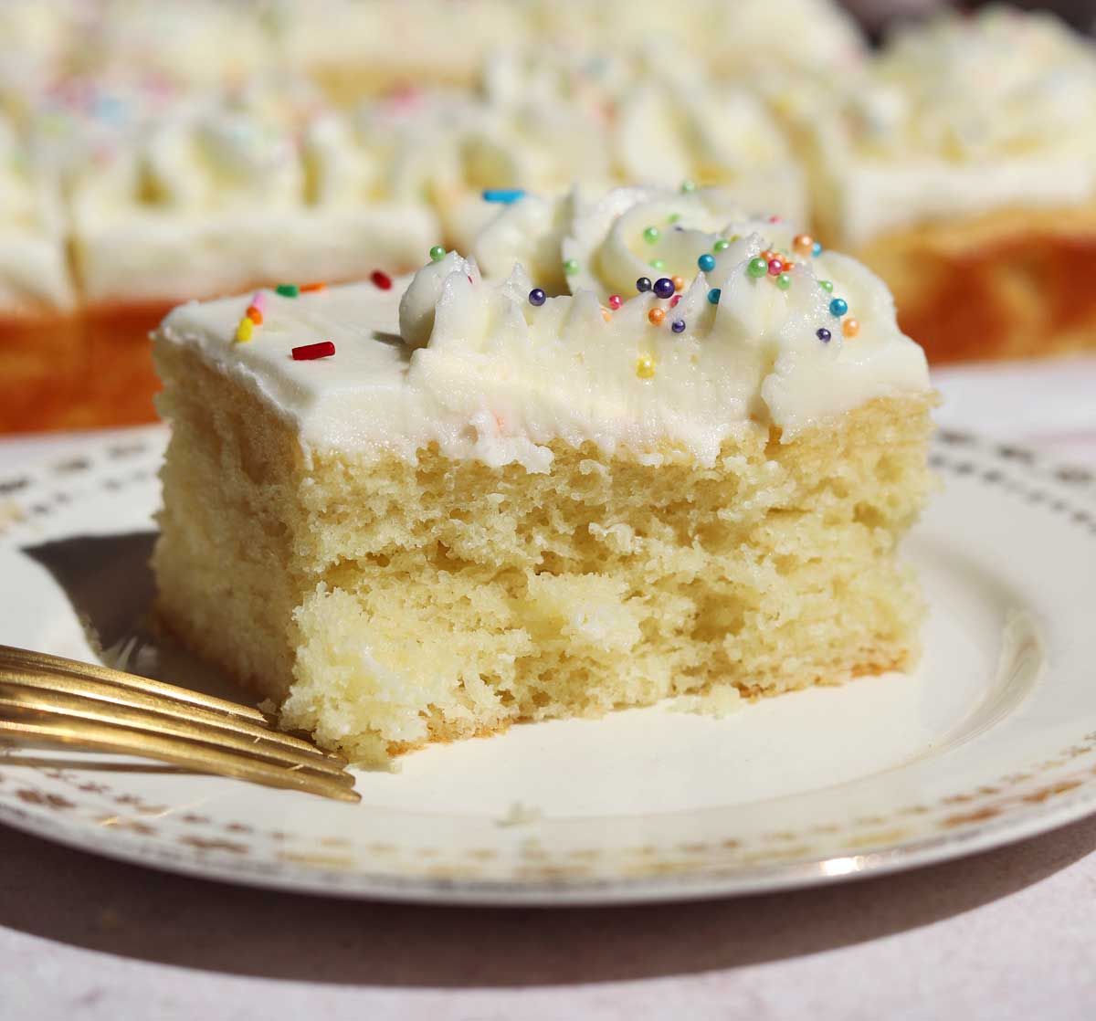 slice of moist vanilla sheet cake on a plate with bite and fork