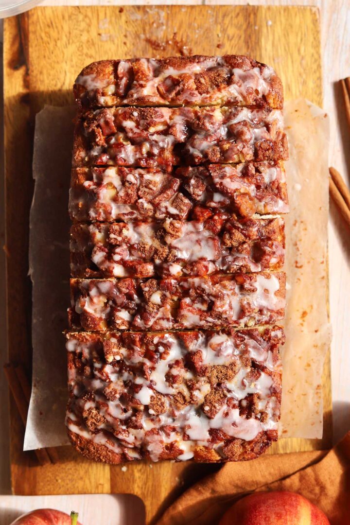 top view of cinnamon apple fritter bread with glaze on a cutting board after baking