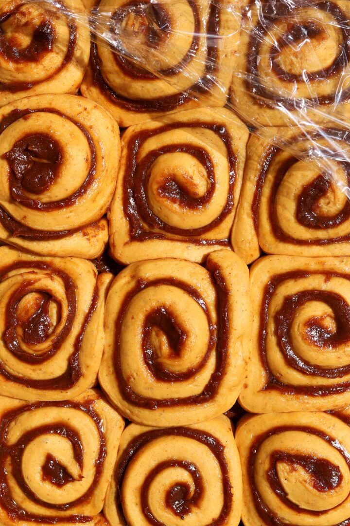 best pumpkin cinnamon roll dough rolled up with pumpkin cinnamon filling in baking pan after proofing