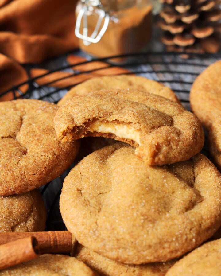 pumpkin cheesecake cookies piled up on cooling rack with bite showing cheesecake filling