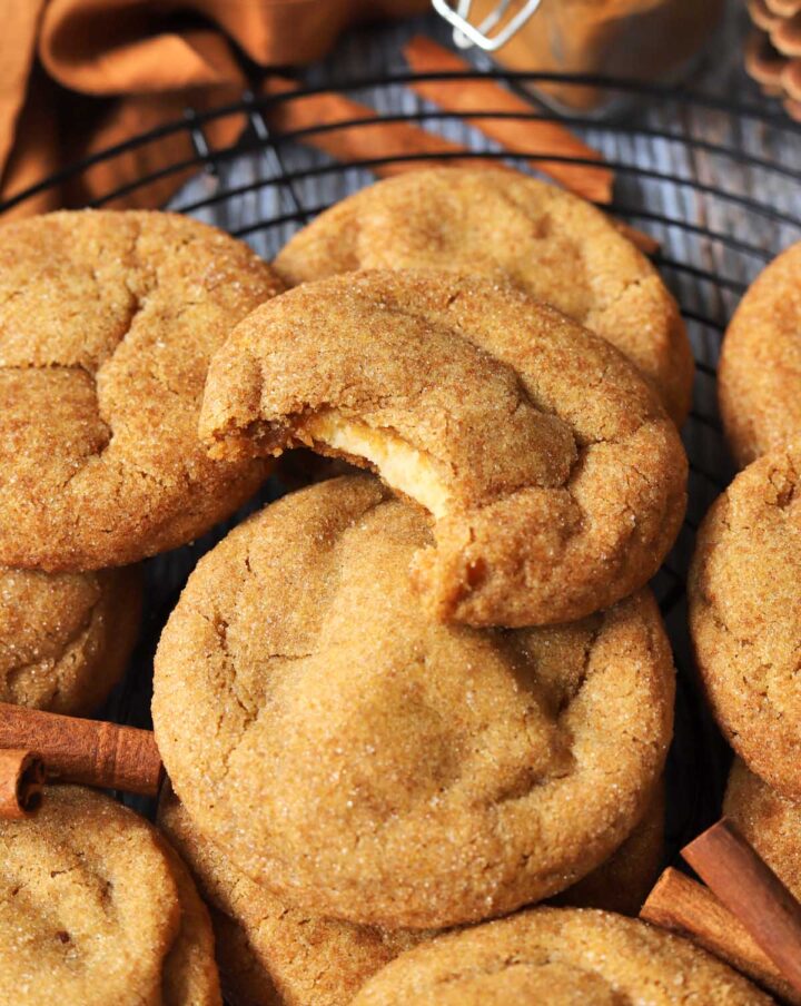 pumpkin cheesecake cookies piled up on cooling rack with bite showing cheesecake filling