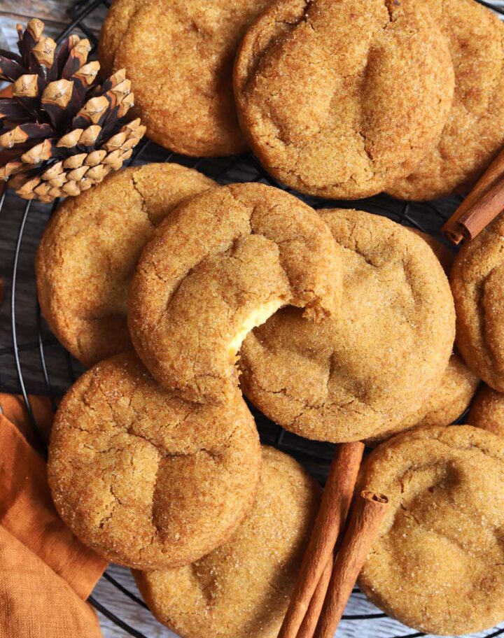 top view of pumpkin cheesecake cookies piled up on cooling rack with bite showing cheesecake filling