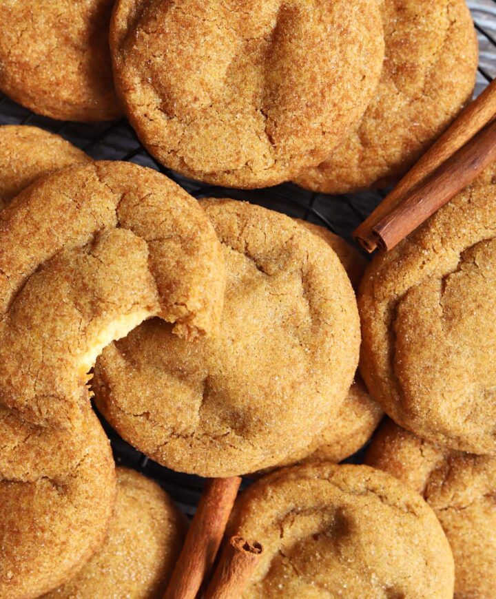pumpkin cheesecake cookies piled up on cooling rack with bite showing cheesecake filling