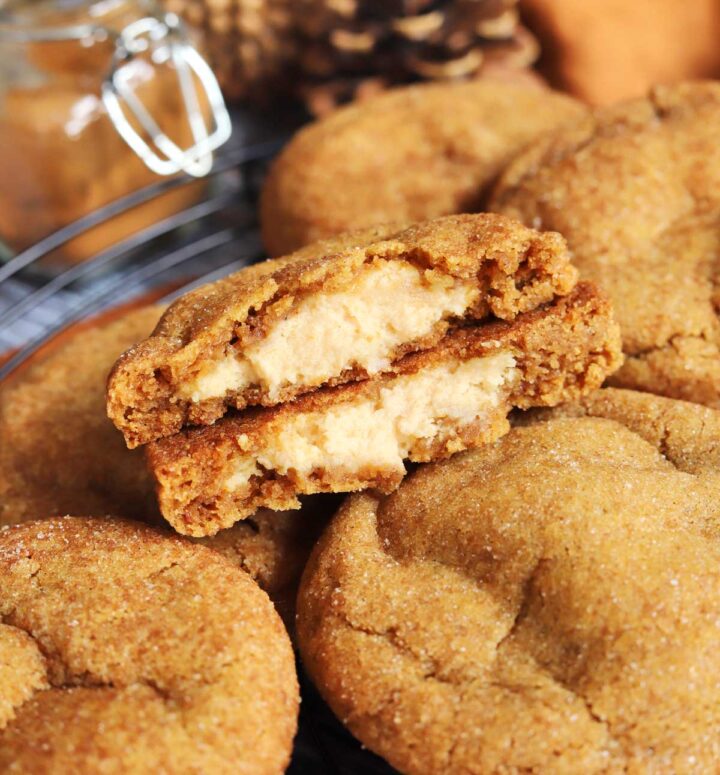 pumpkin cheesecake cookies piled up on cooling rack with cookie split in half showing creamy cheesecake filling